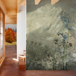 Carta da parati artistica stile vintage denominata Non ti scordar di me: su uno sfondo beige effetto tela grezza con scritte in calligrafia corsiva e la sagoma sfumata di una montagna, spiccano in primo piano vividi fiori azzurri di myosotis e steli essiccati.