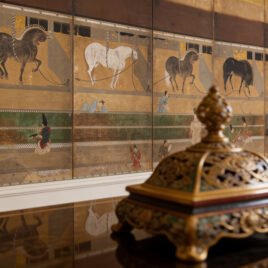 Dettaglio della carta da parati materica Umaya-zu. Un possente cavallo scuro a riposo nel suo stallo, dipinto con tratti antichi su un fondo color oro spento e bruno bruciato, che ricorda un antico paravento giapponese.